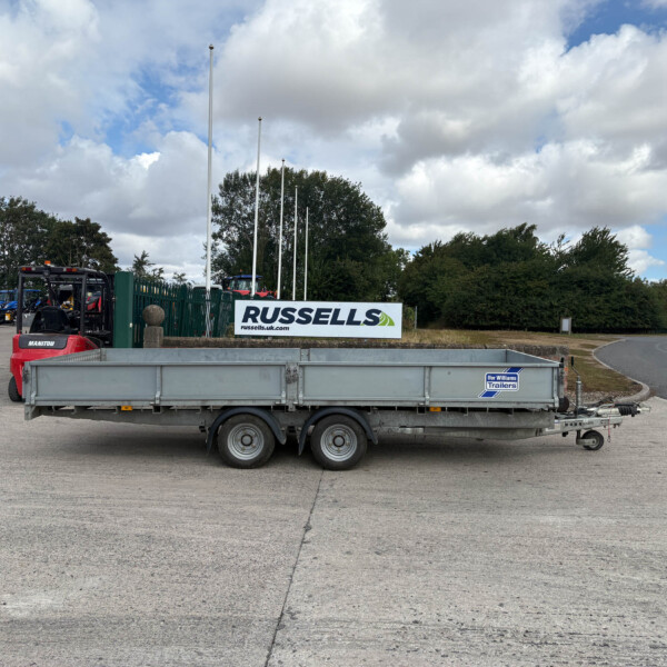 Flatbed trailer in an industrial yard with a Russell's sign and equipment in the background, under a cloudy sky.