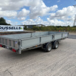 A large metal trailer parked on a paved lot beside a Russell's sign reading russells.uk.com in the foreground.