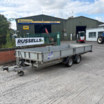 Industrial workshop with Russell's sign, a blue New Holland tractor to the right, and a trailer in the foreground.