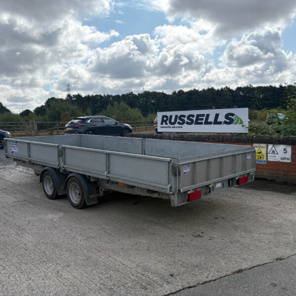 Grey flatbed trailer in a parking lot with a Russell's advertisement sign in the background; blue sky and clouds overhead.