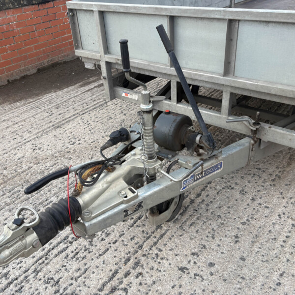 Close-up of a trailer hitch and coupling on a metal trailer frame beside a brick wall.