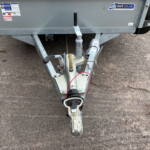 Close-up of a trailer hitch and coupler on a gray utility trailer, with safety chains and a wheel visible in the background