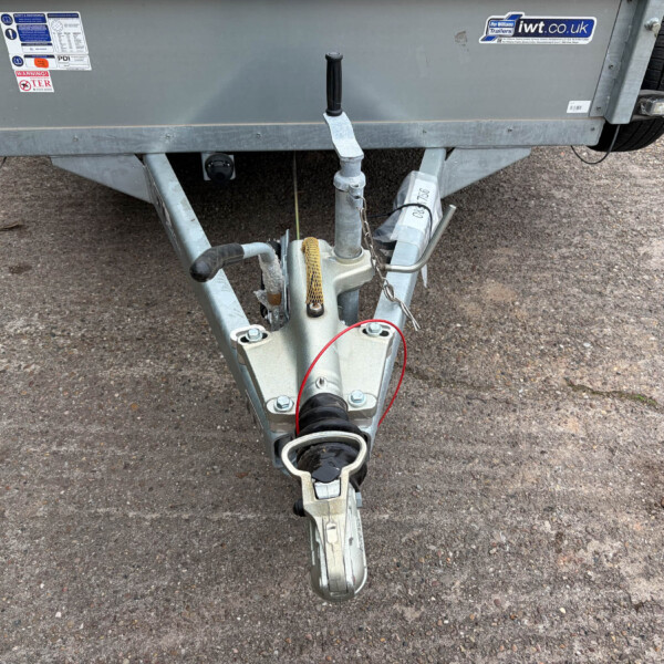 Close-up of a trailer hitch and coupler on a gray utility trailer, with safety chains and a wheel visible in the background
