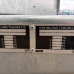 Two Ifor Williams trailer data plates mounted on a weathered metal surface, showing weights and serial numbers.