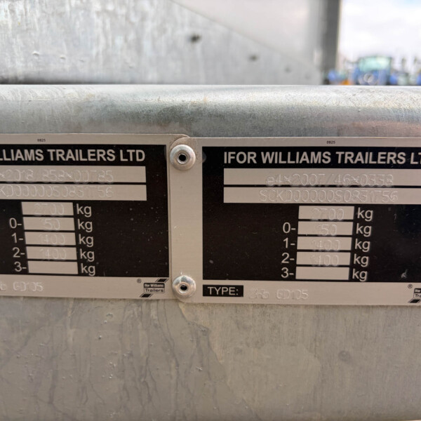 Two Ifor Williams trailer data plates mounted on a weathered metal surface, showing weights and serial numbers.