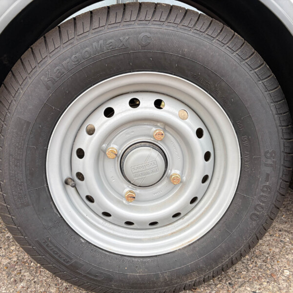 Close-up of a black tire mounted on a silver steel wheel with lug nuts on a rough pavement surface