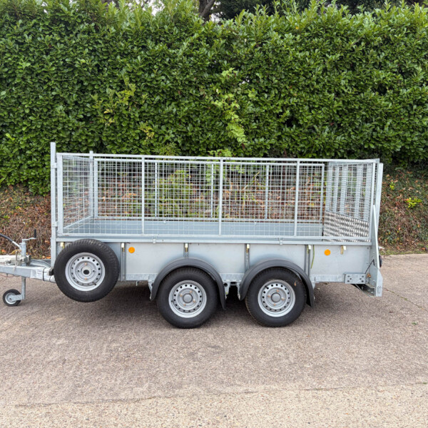 Metal utility trailer with tall wire mesh sides on a paved road, hedge behind it.