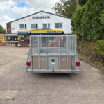 Rear of a metal utility trailer in a parking lot, with a Russell's farm supply store and white building in the background.