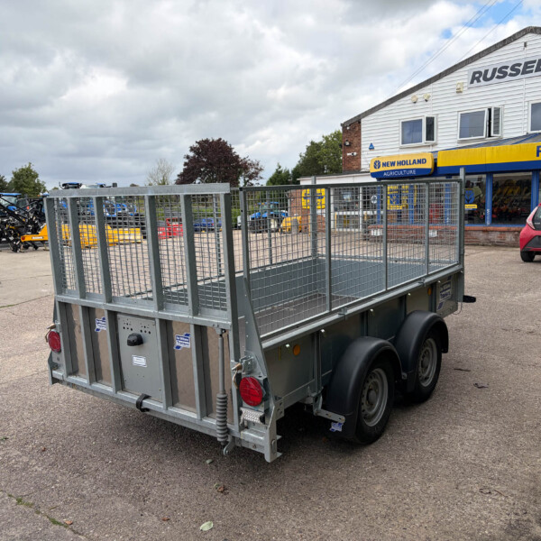 Metal trailer in foreground outside a farm equipment shop, with Russell's signage and a blue-and-yellow New Holland Agriculture store facade in the background
