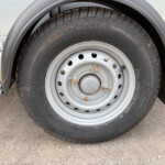 Close-up of a trailer tire mounted on a silver steel wheel with lug nuts and a gray fender above the wheel well.