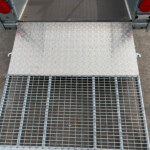 Diamond-plate loading ramp attached to a trailer, seen from above with red tail lights on each side