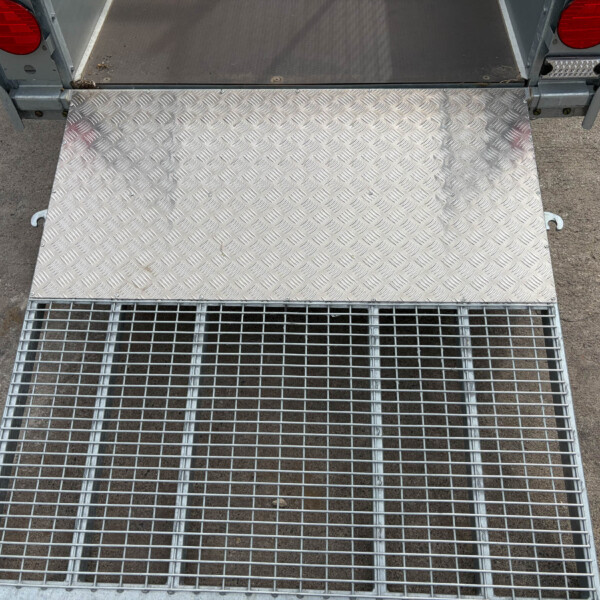 Diamond-plate loading ramp attached to a trailer, seen from above with red tail lights on each side