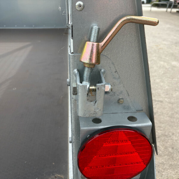 Close-up of a trailer's red tail light with metal frame, latch, and bolts (rear corner view).