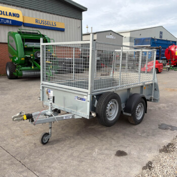 Industrial yard with a metal trailer in foreground and agricultural equipment parked at a New Holland sign building