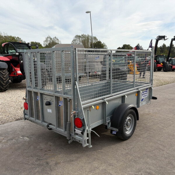 Metal mesh-sided trailer in a dealership yard with red tractors visible in the background.
