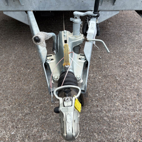 Close-up of a silver trailer hitch and jack assembly with a frayed protective cover on a gravel surface.