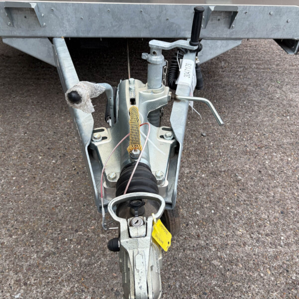 Close-up of a trailer hitch showing the coupler, tongue jack, safety chains, and wiring on a gravel surface.