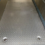 Diamond-plate metal floor with circular access holes and metal side walls; a few leaves scattered across the surface.