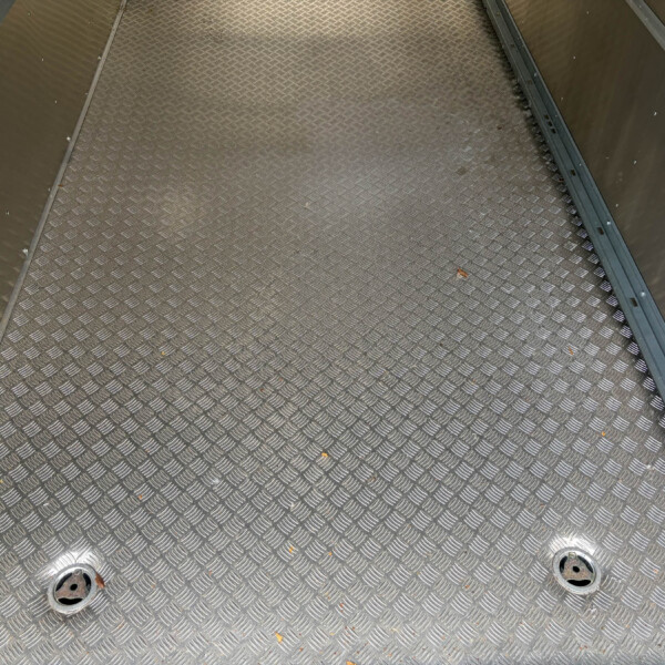 Diamond-plate metal floor with circular access holes and metal side walls; a few leaves scattered across the surface.