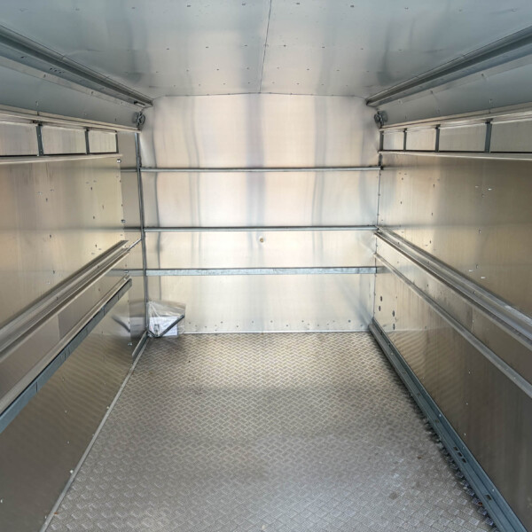 Interior of an empty aluminum cargo trailer with riveted silver walls and a diamond-plate floor.