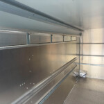 Interior of a empty metal trailer with riveted aluminum walls and track rails along the sides, diamond-plate floor visible