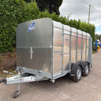 Long silver metal trailer with a rounded roof, parked on a street beside a hedge; Ifor Williams Trailers logo visible.