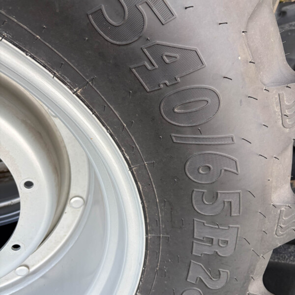Close-up of a large black tire with raised lettering (Goodyear) beside a silver wheel rim, showing tread details and edge of the rim.