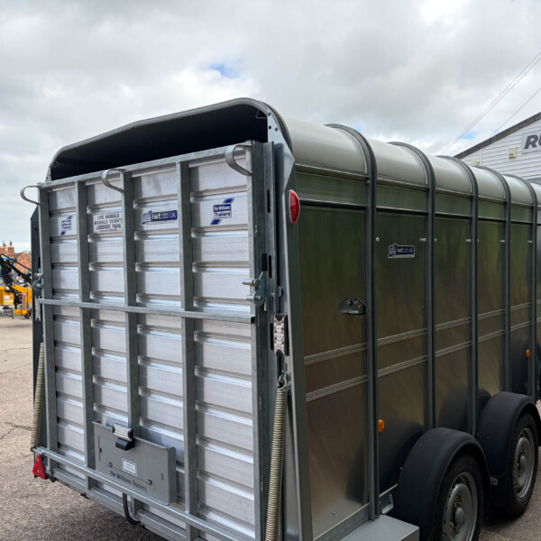 Rear of a metal livestock trailer with a curved roof and twin axles parked in a dealership lot, with a Russell building in the background.
