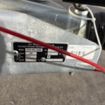 Close-up of a silver metal trailer hitch/frame with an identification plate reading 'IFOR WILLIAMS' and red and white cables crossing the scene in the foreground.