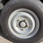 Close-up of a black tire mounted on a gray steel wheel with visible lug nuts in a vehicle wheel well.