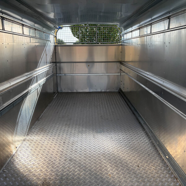 Empty aluminum cargo trailer interior with diamond-plate floor and mesh rear gate exposing trees outside.