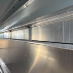 Interior of a metal truck trailer with riveted panels and a perforated vent on the left, looking down the empty cargo area.