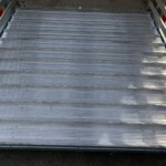 Top-down view of ribbed aluminum stairs on a loading platform with side rails and a dark ground below.