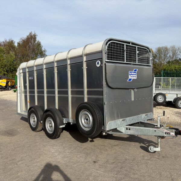 Three-axle gray livestock trailer with rounded roof panels and metal ventilation grid, parked in an outdoor yard.