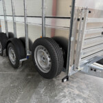 Side view of a metal utility trailer with dual wheels, silver aluminum rails, and fenders near the ground.