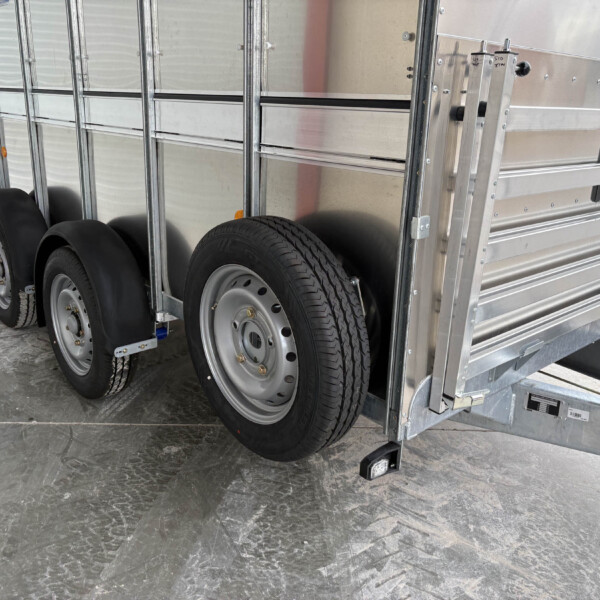 Side view of a metal utility trailer with dual wheels, silver aluminum rails, and fenders near the ground.
