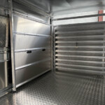 Interior of a metal trailer showing aluminum walls, ribbed panels, and diamond-plate floor with a stair-step rack on the right side (empty loading area).