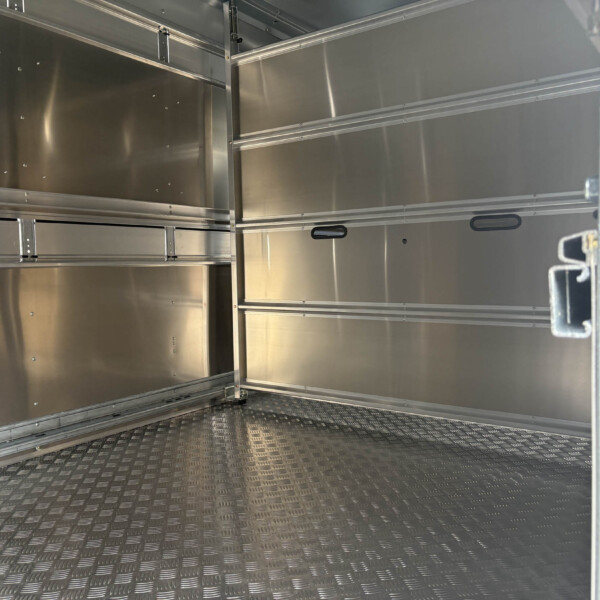 Interior of an empty metal freight trailer with silver walls, horizontal rails, and a diamond-plate floor viewed from the doorway