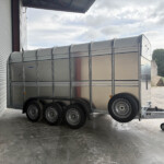 Shiny aluminum multi‑axle cargo trailer parked in a loading bay beside a metal roll‑up door, ready for loading.