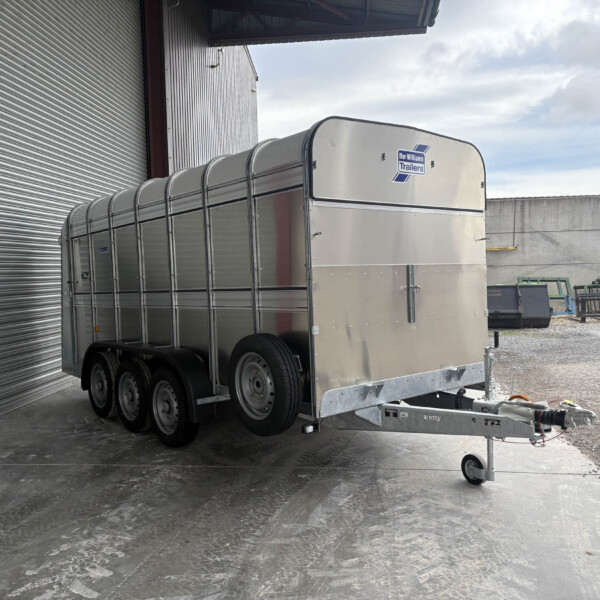 Silver multi-axle aluminum trailer with rounded top panels parked beside a corrugated metal building and roll-up door.
