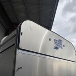 Silver trailer side with door and a Williams Trailers sticker, outdoors under a cloudy sky.