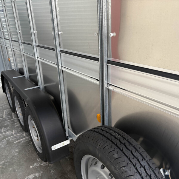Side of a silver utility trailer with metal framing, wheel wells, and two tires visible in the foreground.