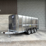 Silver multi-axle trailer with a rounded front parked outside a corrugated metal warehouse featuring a large roll-up door.