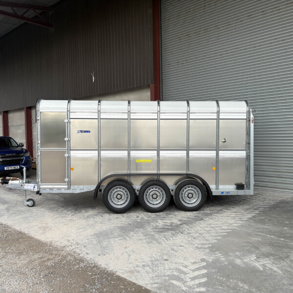 Silver trailer hitched to a blue pickup truck, parked beside a large corrugated metal warehouse with a closed rolling shutter door.