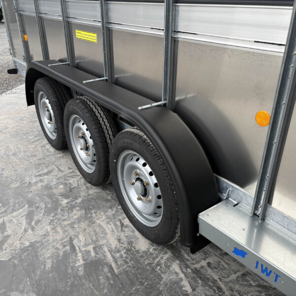 Side view of a metal trailer showing dual wheels, black fenders, orange reflectors, and a yellow warning sticker on the panel edge.