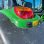 Close-up of a green tractor rear light with orange turn signal and red brake light, black fender nearby.