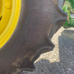 Close-up of a large tractor tire with a bright yellow rim and green farming equipment in the background, showing dirt on the tread.