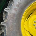 Close-up of a tractor tire with a yellow rim and dirt on the tread, green machinery in the background.