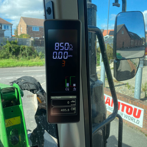 Digital readout in a tractor cab shows 650 n/min and 0.00 MPH, with a large side mirror and residential street visible outside the window.