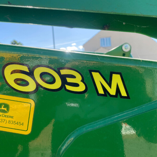 Close-up of green John Deere machinery panel with a yellow warning sticker and partial model/serial numbers (663BM).